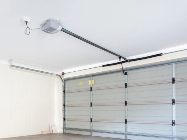 Ceiling-mounted automatic garage door opener with a heavy-duty rail system installed on a light gray sectional door by Greer Garage Doors.