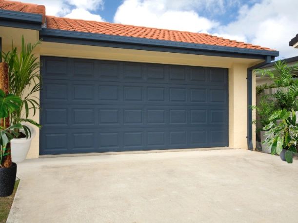 Modern navy blue double garage door with a traditional raised-panel design, providing a bold contrast to a cream-colored home by Greer Garage Doors.