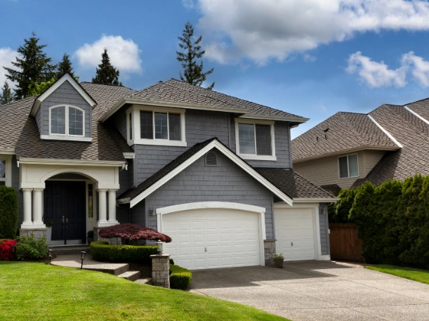 High-end residential garage door replacement featuring white steel doors that complement a modern gray exterior and professional landscaping.