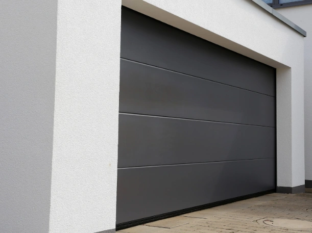 Modern dark charcoal gray flush-panel garage door installed on a minimalist white stucco home by Greer Garage Doors.